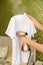 woman irons white t-shirt by portable hand steamer for clothes.