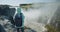 Woman with jacket and backpack standing at cliff edge looking at Detifoss waterfall in Iceland