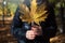 Woman in a jacket holds a large yellow maple leaf