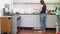 Woman in jeans black tank and with headphones cooks pancakes in kitchen