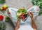 Woman in jeans holding fresh healthy green salad with quinoa, peach, greens, avocado, berries, melon in bowl on light background