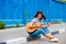 Woman in jeans sits on a road curb and plays the guitar