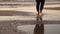 Woman in jeans walking on sandy beach at sunset. Close up of girl feet on the sand lit by golden sun light