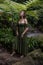 Woman in jungle standing under the fern, wearing green dress. Caucasian woman walking in tropical rain forest. Nature concept.