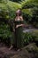 Woman in jungle standing under the fern, wearing green dress. Caucasian woman walking in tropical rain forest. Nature concept.