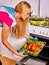 Woman in kitchen is cooking roast meat food in oven.