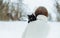 A woman in a knitted sweater with a black cat on her shoulder stands on a snowy street