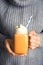 Woman in knitted sweater holding mason jar with pumpkin spice latte and whipped cream