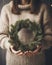 Woman in knitted sweater holds green Christmas wreath in hands.