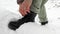 A woman laces up black winter boots on a street in a snowy forest. Women\\\'s hands tie shoelaces, winter shoes.