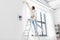 woman on ladder hanging curtains at home