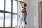 woman on ladder hanging curtains at home