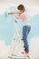 Woman on ladder painting wall with paint roller