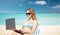 Woman with laptop sunbathing in lounge on beach