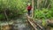 A woman with a large backpack crosses a mountain river in the forest on logs.