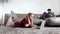 Woman laying on carpet looking at laptop while man sitting on couch reading book