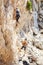 Woman lead climbing on natural cliff, guy belayer watching her