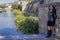 Woman leaning against a stone wall with a brook and fountain background