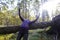 Woman leans over fallen tree and rised her hands towards sun