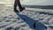 A woman in leather boots walks along a slippery embankment covered with ice and snow on a sunny day in early winter