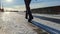 A woman in leather boots walks along a slippery embankment covered with ice and snow on a sunny day in early winter