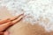 Woman legs on the beach with foam waves. Closeup detail of female feet and golden sand, sea waves during tanning session