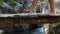 Woman legs walking on wooden bridge across stony river in mountains. Close up barefoot woman walking along hanging