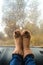 Woman legs in warm cute socks on car dashboard. Drinking warm tee on the way. Fall trip. Rain drops on windshield. Freedom travel