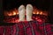 Woman legs in winter white socks covered christmas plaid near fireplace flame.