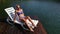Woman lie on a sunbed in sunglasses and swimming suit. Girl rest on a flood wood underwater pier. The pavement is