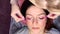A woman lies with her eyes closed in a beauty procedure. The master combs the extension eyelashes with a pink brush. Top