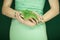 Woman in light green dress with green nail polish, hands holding some tropical leaves