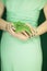 Woman in light green dress with green nail polish, hands holding some tropical leaves