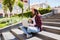 Woman with limonade sitting on the city stairs and using laptop