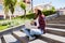 Woman with limonade sitting on the city stairs and using laptop