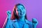 Woman listening to music via headphones, keeps eyes closed and happy smiling, keeping fists raising isolated over pink neon