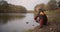 Woman and little boy are throwing stone in water on shore of river in forest, family time together at weekend at autumn