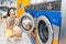 Woman loading dirty clothes in washing machine in laundromat, laundry service concept