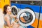 Woman loading dirty clothes in washing machine in laundromat, laundry service concept