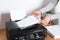 Woman loading paper into printer at wooden table indoors, closeup