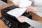 Woman loading paper into printer at wooden table indoors, closeup