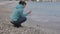 Woman at lonely cold beach. Attractive caucasian woman playing with stones near the water on the beach.