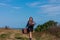 Woman with long brown hair in denim jacket, black skirt, vintage suitcase, flowers bouquet off-road. Lifestyle photo