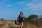 Woman with long brown hair in denim jacket, black skirt, vintage suitcase, flowers bouquet off-road. Lifestyle photo