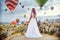 Woman in a long dress on background of balloons in Cappadocia. Girl with flowers hands stands on a hill