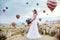 Woman in a long dress on background of balloons in Cappadocia. Girl with flowers hands stands on a hill and looks