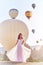 Woman in a long dress on background of balloons in Cappadocia. Girl with flowers hands stands on a hill and looks at large number