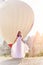 Woman in a long dress on background of balloons in Cappadocia. Girl with flowers hands stands on a hill and looks at large number