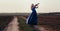 Woman in long dress playing violin on background of field path with a club of dust, girl engaged in musical art, performance on