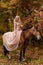 A woman in a long dress sits on a horse. Autumn forest, horse breeding